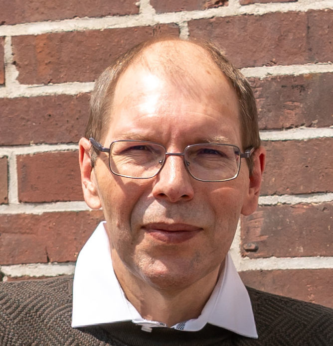 Der erfolgreiche Umschüler André Pardun steht mit verschränkten Armen vor einer geziegelten Hauswand.