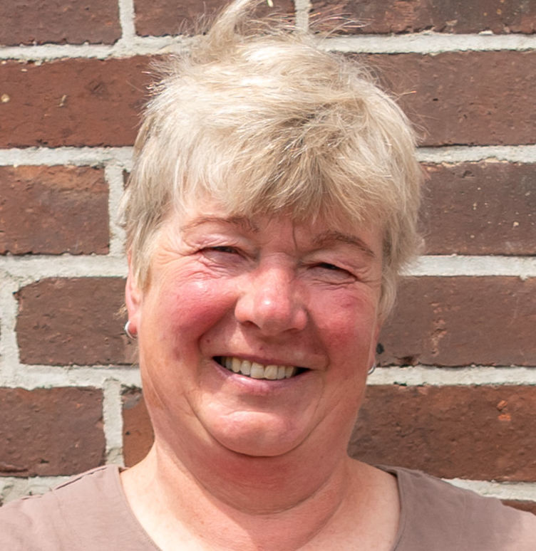 Die stolze Weiterbildungsteilnehmerin Astrid Estel steht, die Hände auf die Hüften gestützt, vor einer geziegelten Hauswand.